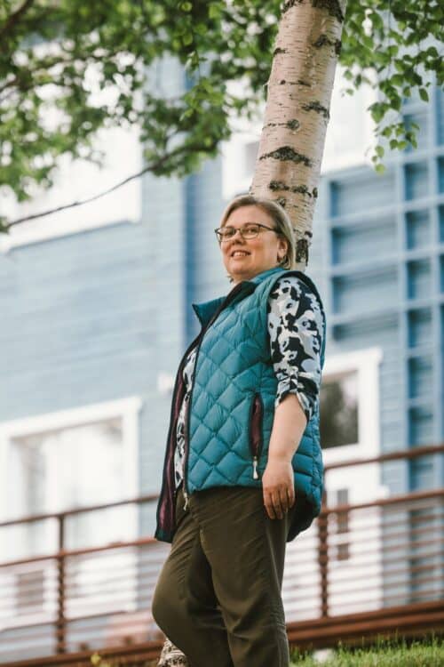 Irina Karppinen seisomassa hotellinsa takana koivun alla.
