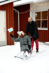 Katja ja Richard punaisen talon edessä, Katja heiluttaa Suomen lippua.